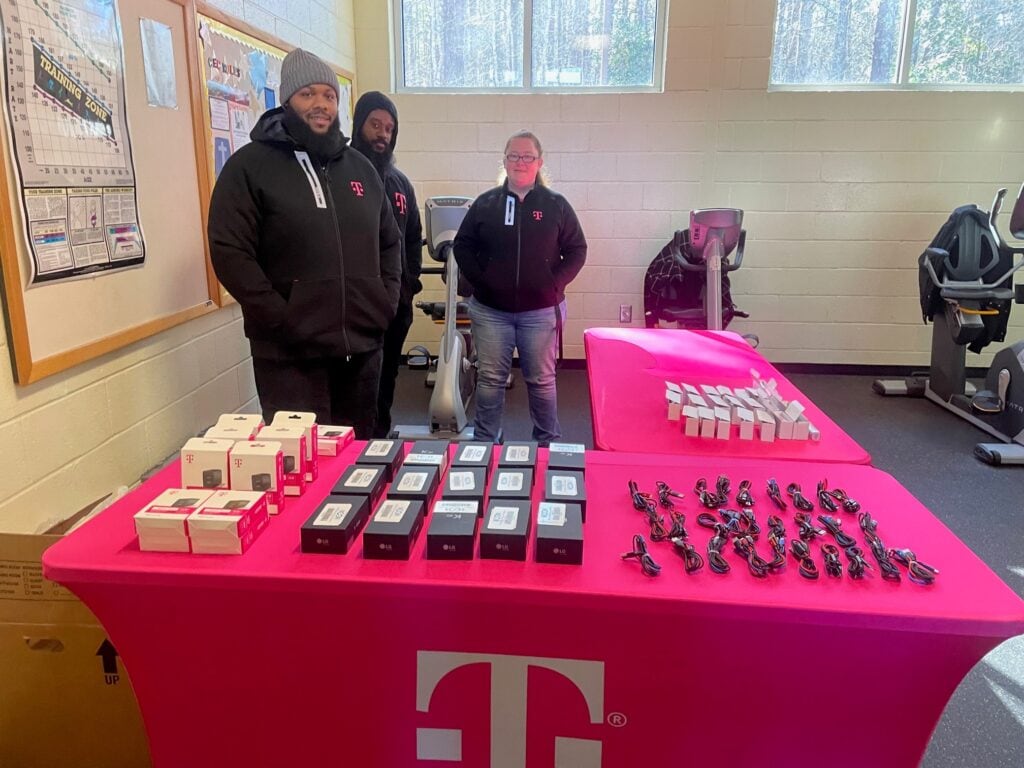 Two men and one female standing behind a T-Mobile branded table passing out hotspots in a gym facility