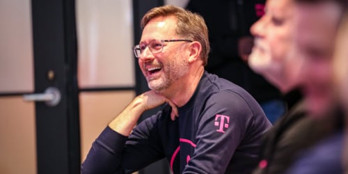 Image of T-Mobile CEO, Mike Sievert smiling wearing a black shirt with T-Mobile logo on the shoulder.